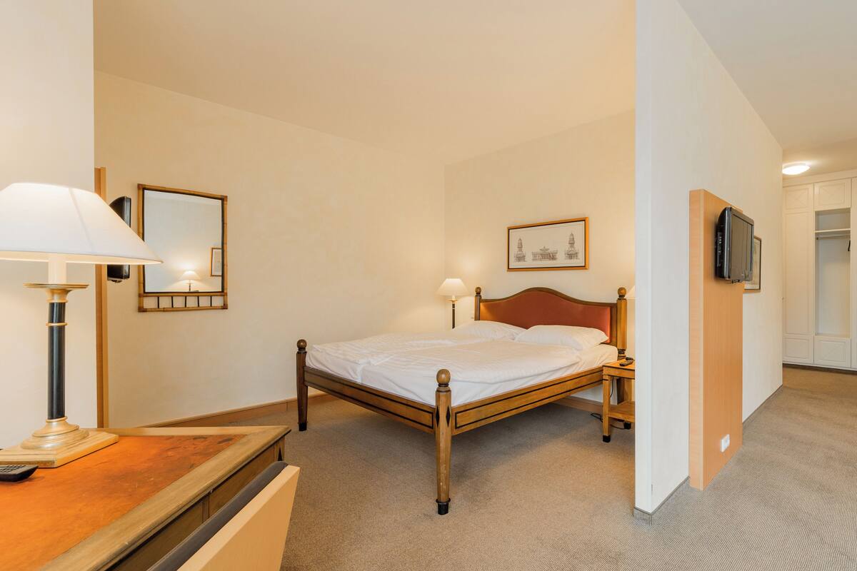 A neatly arranged hotel room with a single bed, bedside tables, a lamp, a framed picture on the wall, and a television mounted on the wall.
