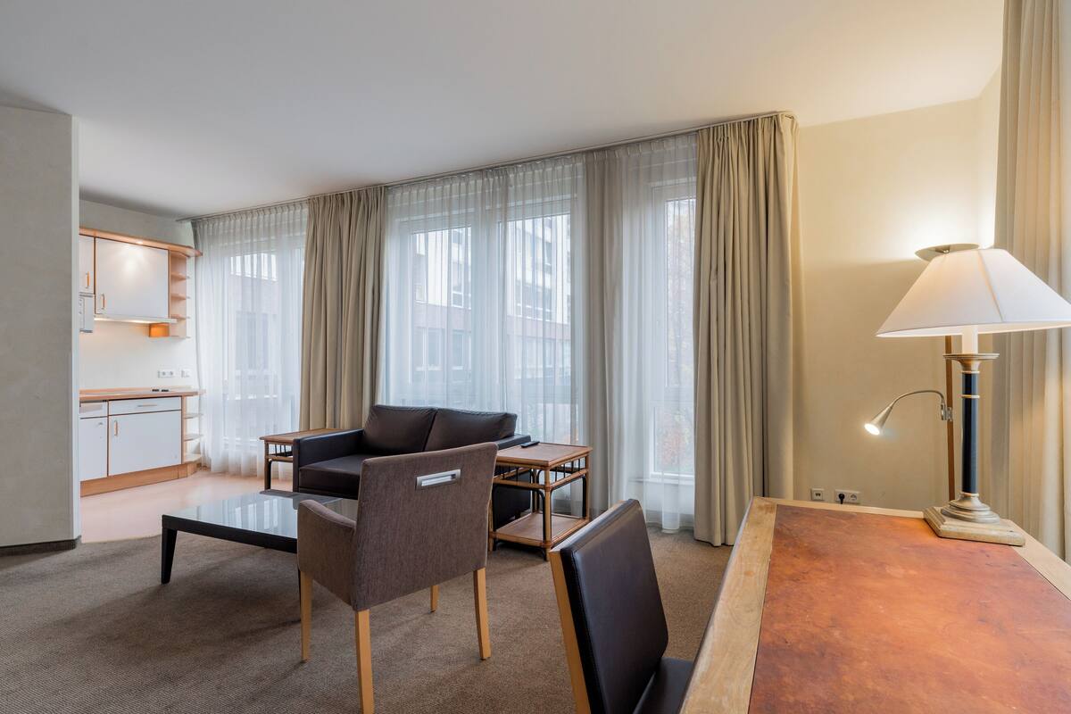 A modern hotel room with a dining area, a sofa, a coffee table, and a lamp.
