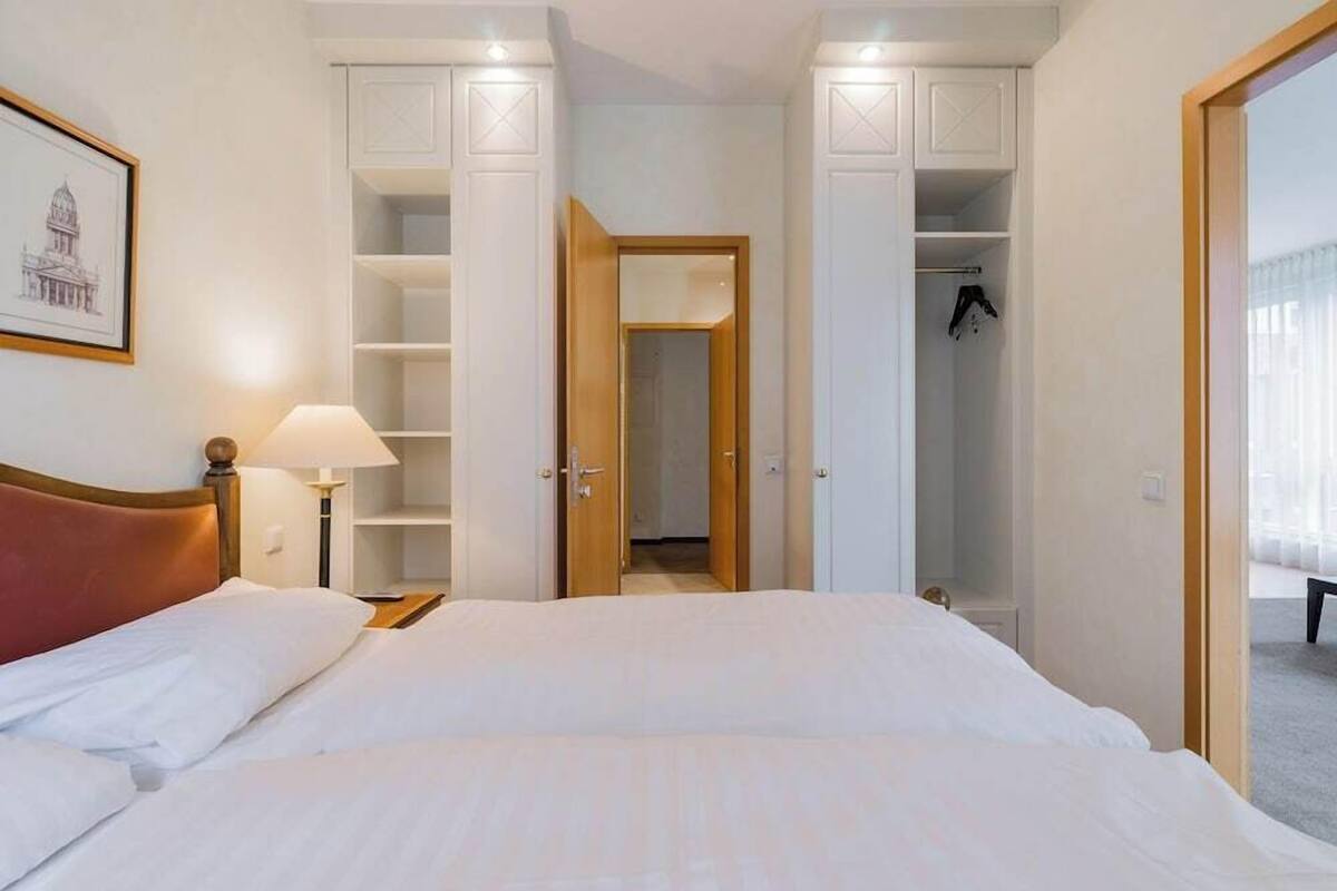A hotel room with a bed, a nightstand, a lamp, a wardrobe, and a door leading to a bathroom.