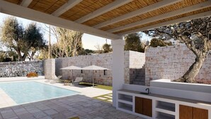 A covered outdoor area with a swimming pool, seating, and a stone wall.
