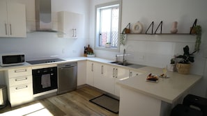 A modern kitchen with white cabinets, stainless steel appliances, a window with plants, and a small island with food and a glass.