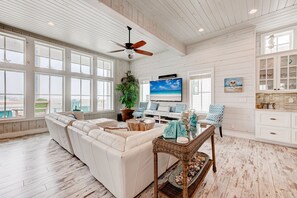 A spacious living room with a large white sofa, a dining table with decorative items, and a view of the ocean through large windows. - HOUSE of VIEWS is without a doubt one of the most luxurious and expansive vacati (Port Aransas)