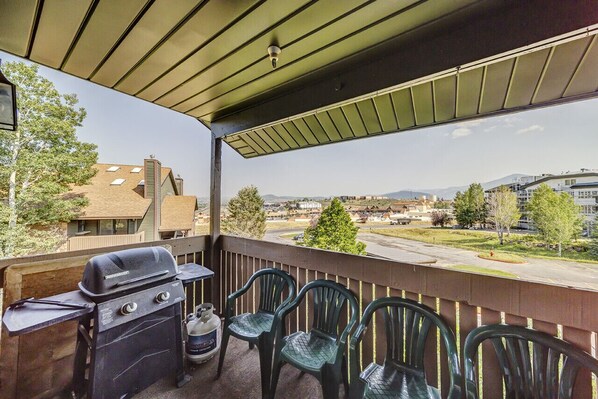 Un balcón con una parrilla, sillas y vistas a un paisaje urbano.