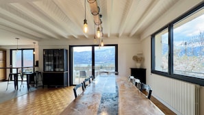 A spacious dining area with a long table, chairs, and a view of mountains through large windows.