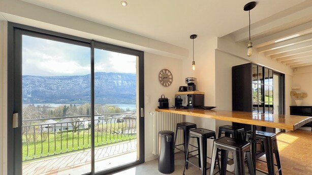A modern kitchen with a wooden countertop, black bar stools, and a view of mountains through large sliding glass doors.