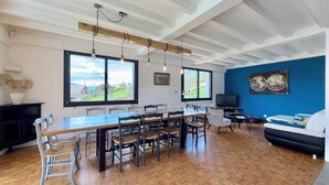A spacious living area with a large wooden dining table, multiple chairs, a sofa, a television, and a world map artwork on the wall.