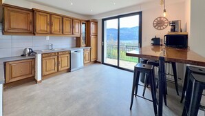 A modern kitchen with wooden cabinets, a dishwasher, a coffee machine, and a large window with a view of hills.