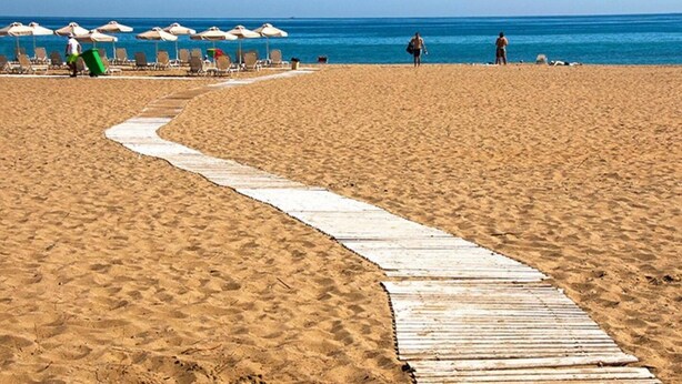 A sandy beach with a wooden boardwalk leading to beach umbrellas and lounge chairs. - Stunning 3-bedroom Villa Near Malia Beach (Agios Nikolaos)
