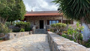 A stone pathway leading to a house with a tiled roof, surrounded by greenery and a stone wall. - Stunning 3-bedroom Villa Near Malia Beach (Agios Nikolaos)