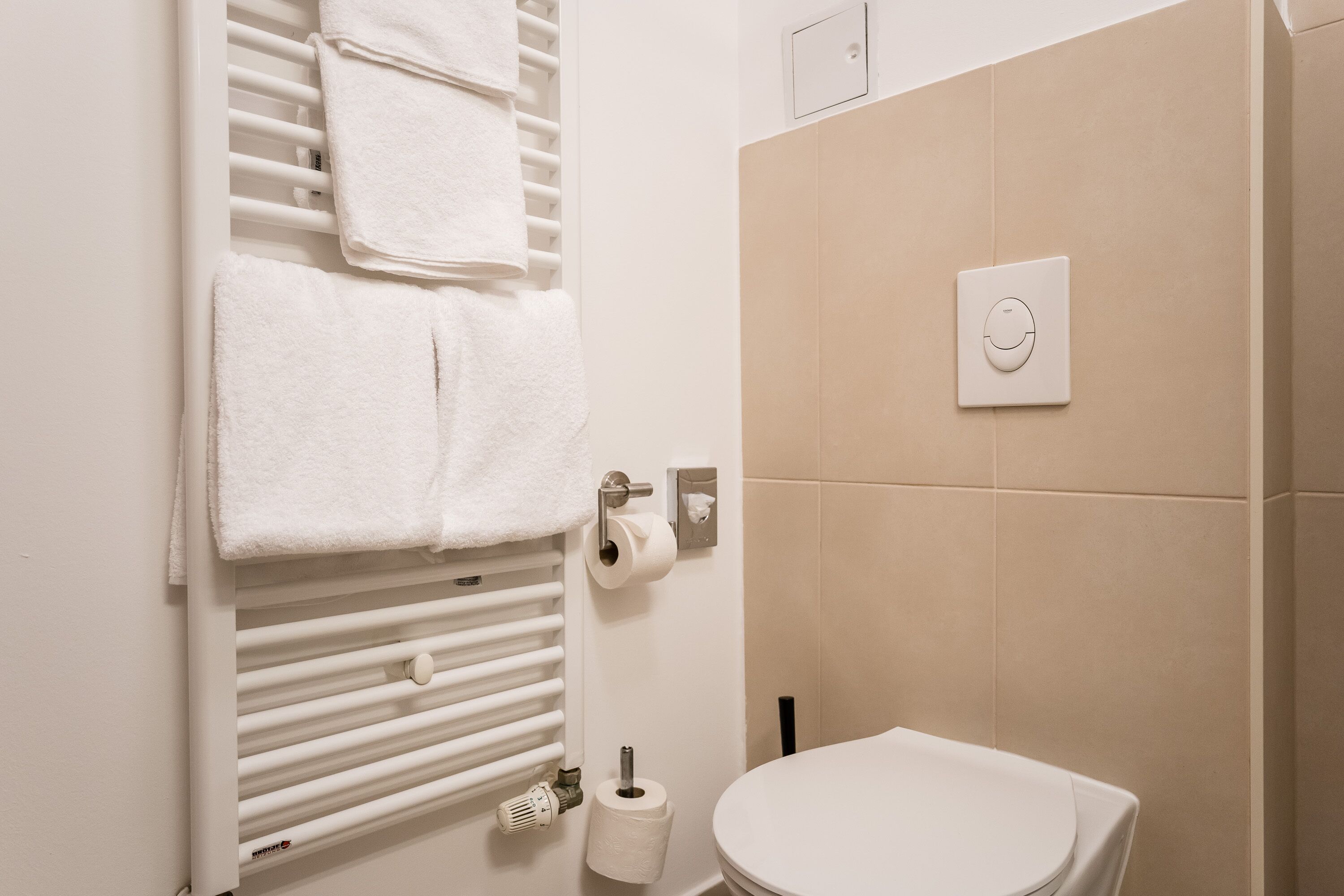 Un baño con inodoro, toallero y termostato en la pared.