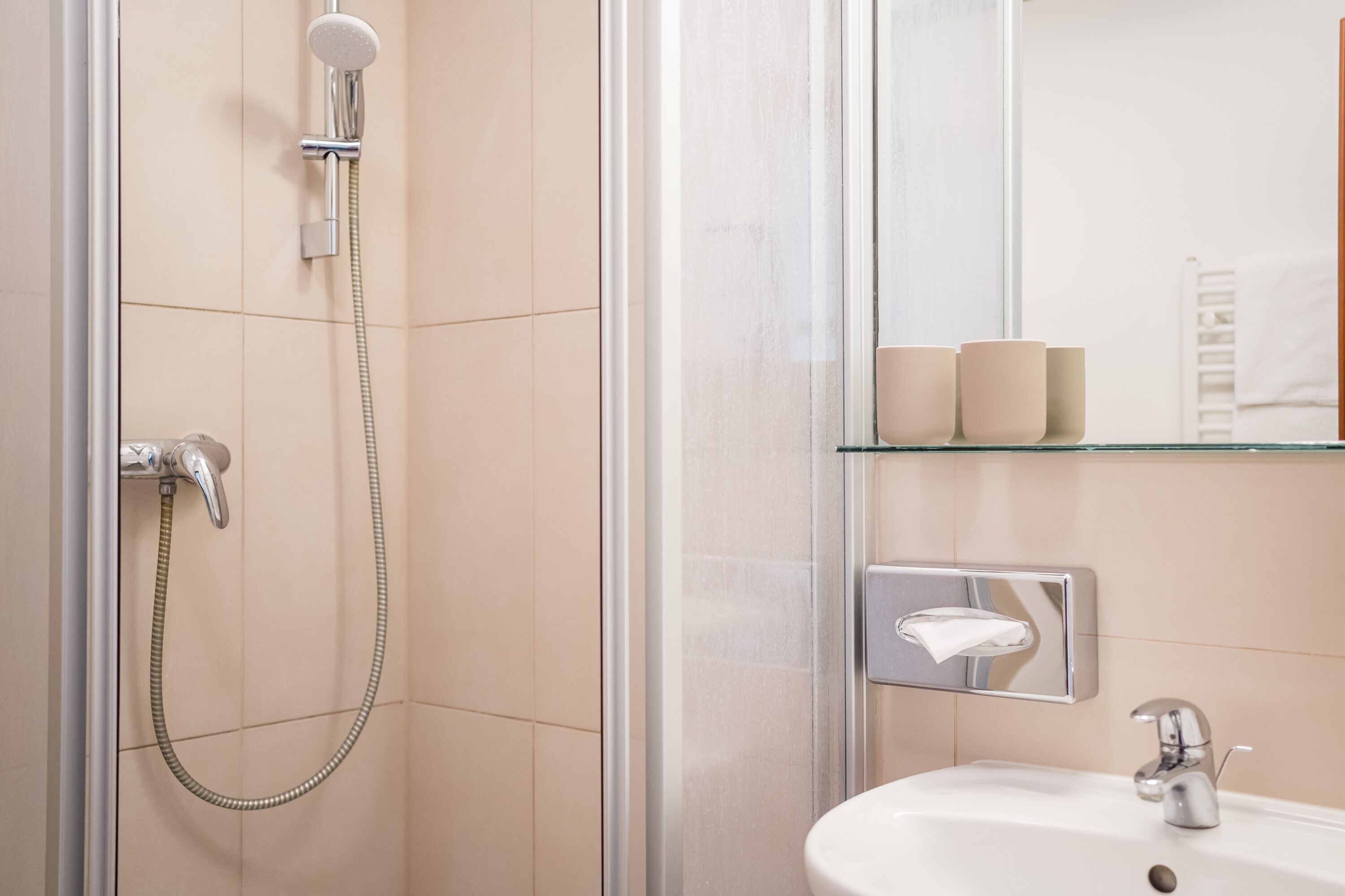 Een badkamer met een douchecabine van glas, een witte wastafel en een zakdoekdispenser.