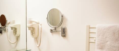 A bathroom with a hairdryer, a mirror, a towel rack, and a soap dispenser.