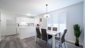 Une cuisine moderne avec des meubles blancs, une table à manger avec des chaises et un luminaire suspendu.