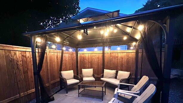 Une terrasse extérieure dotée d’un espace salon couvert, d’une table et d’une pergola agrémentée de guirlandes lumineuses.