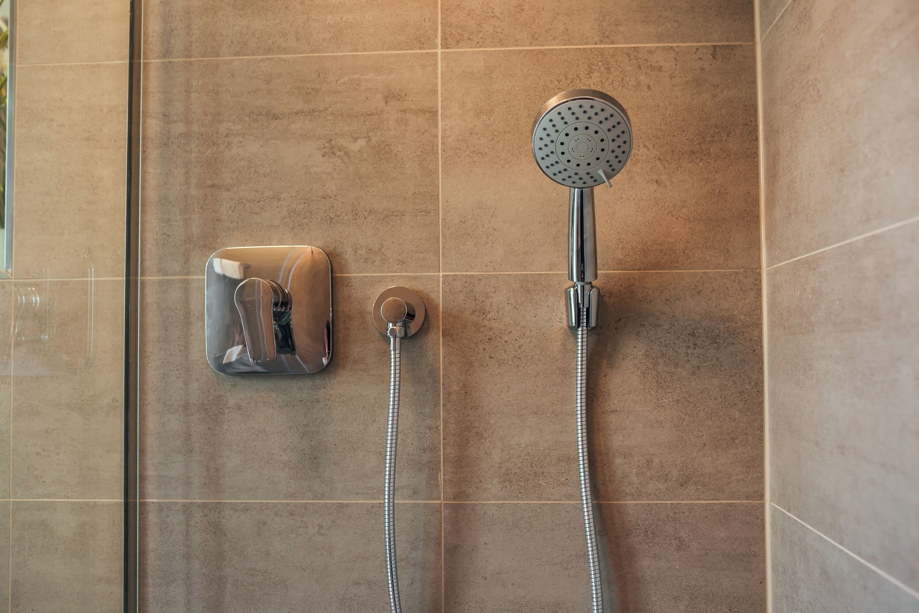 A shower with a handheld showerhead and a wall-mounted control.