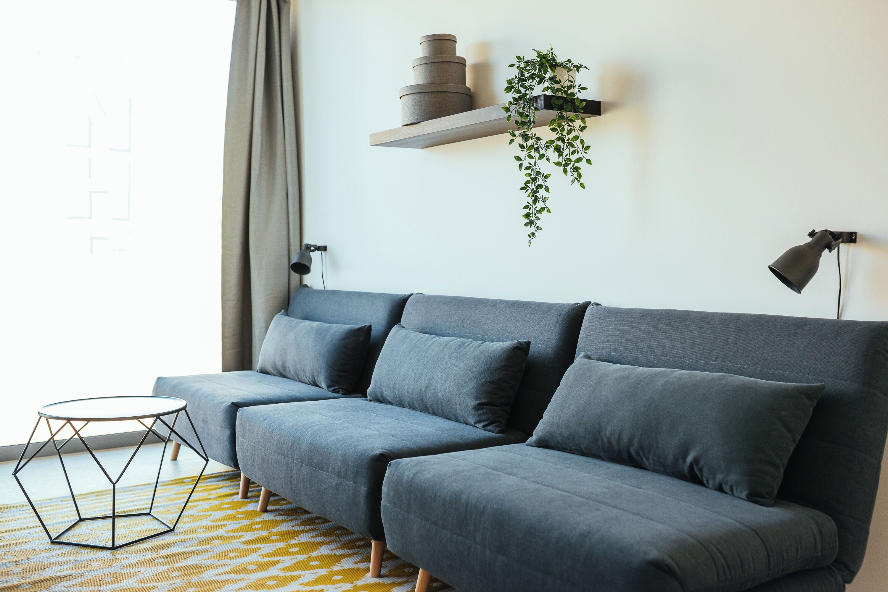 Ein modernes Wohnzimmer mit einem grauen Sofa, einem kleinen runden Tisch und einer hängenden Pflanze.