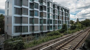 Ein modernes Gebäude mit einer rasterförmigen Fassade, großen Fenstern und einem Gleis in der Nähe.