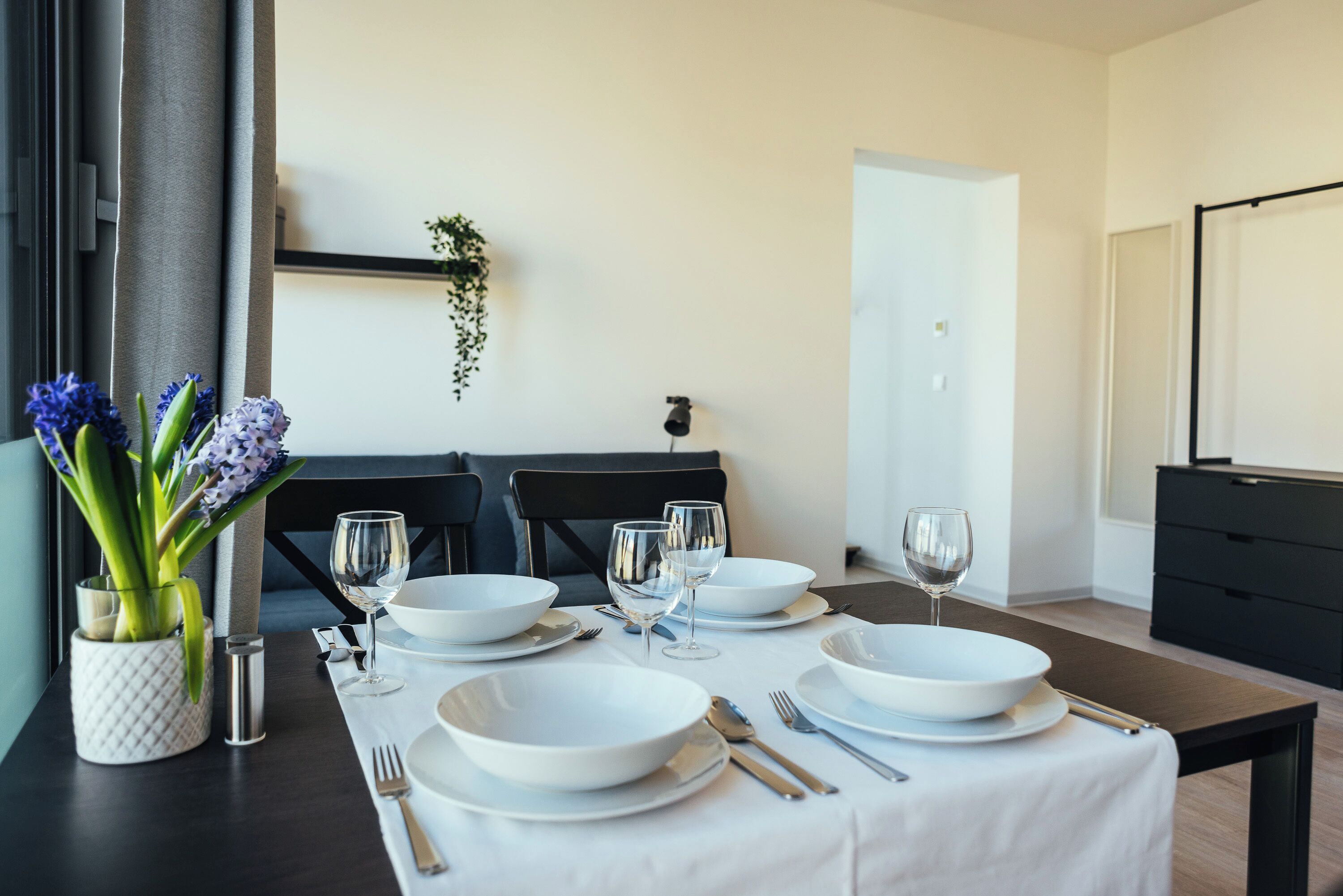 A dining table set with white plates, bowls, and cutlery, a vase with flowers, and a dark wooden table.