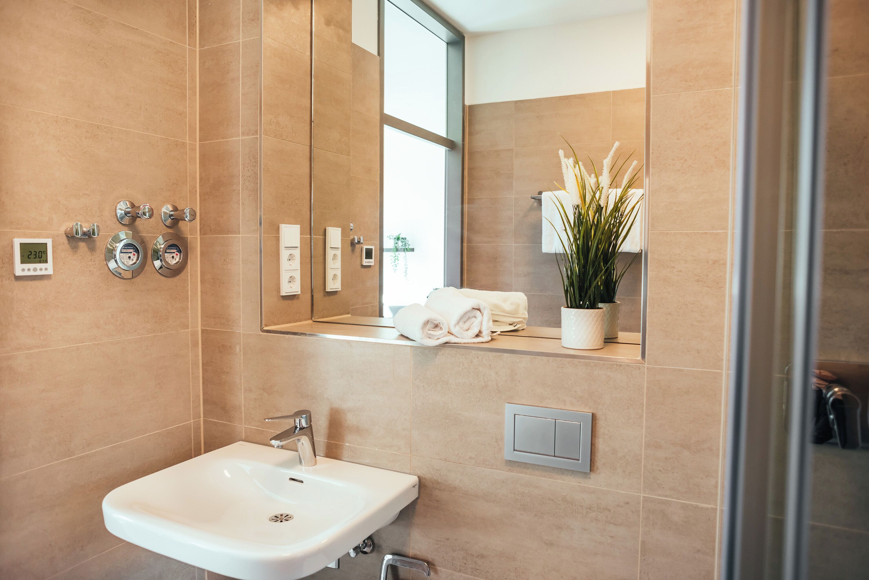 Ein modernes Badezimmer mit einem weißen Waschbecken, einem großen Spiegel und einer Topfpflanze.