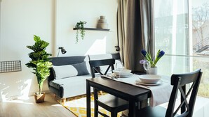 Un soggiorno moderno con divano, tavolo da pranzo e sedie. Si nota una pianta in vaso, un vaso con fiori e uno scaffale con oggetti decorativi.