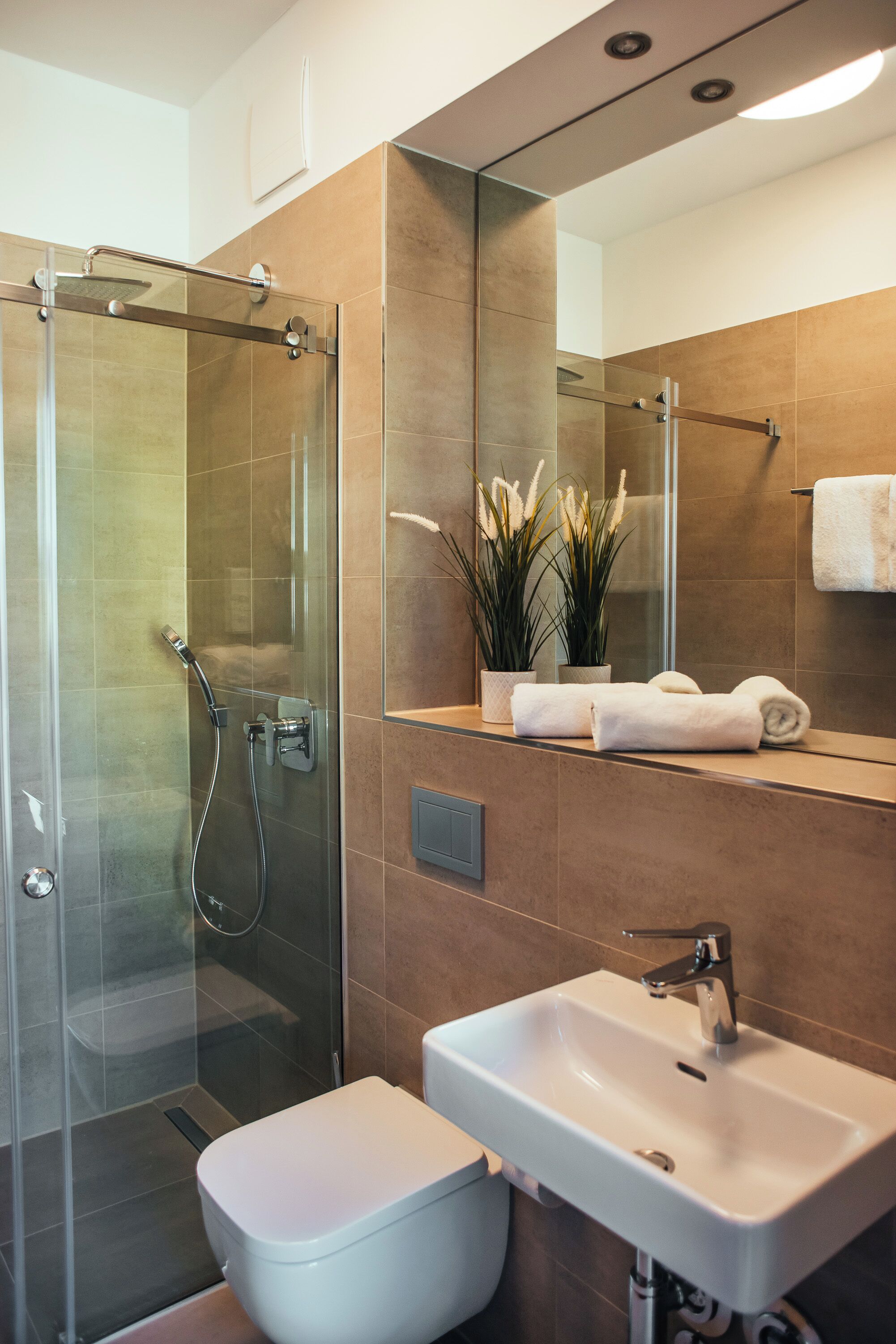 Un baño moderno con ducha envuelta en vidrio, un lavamanos blanco y un espejo grande.