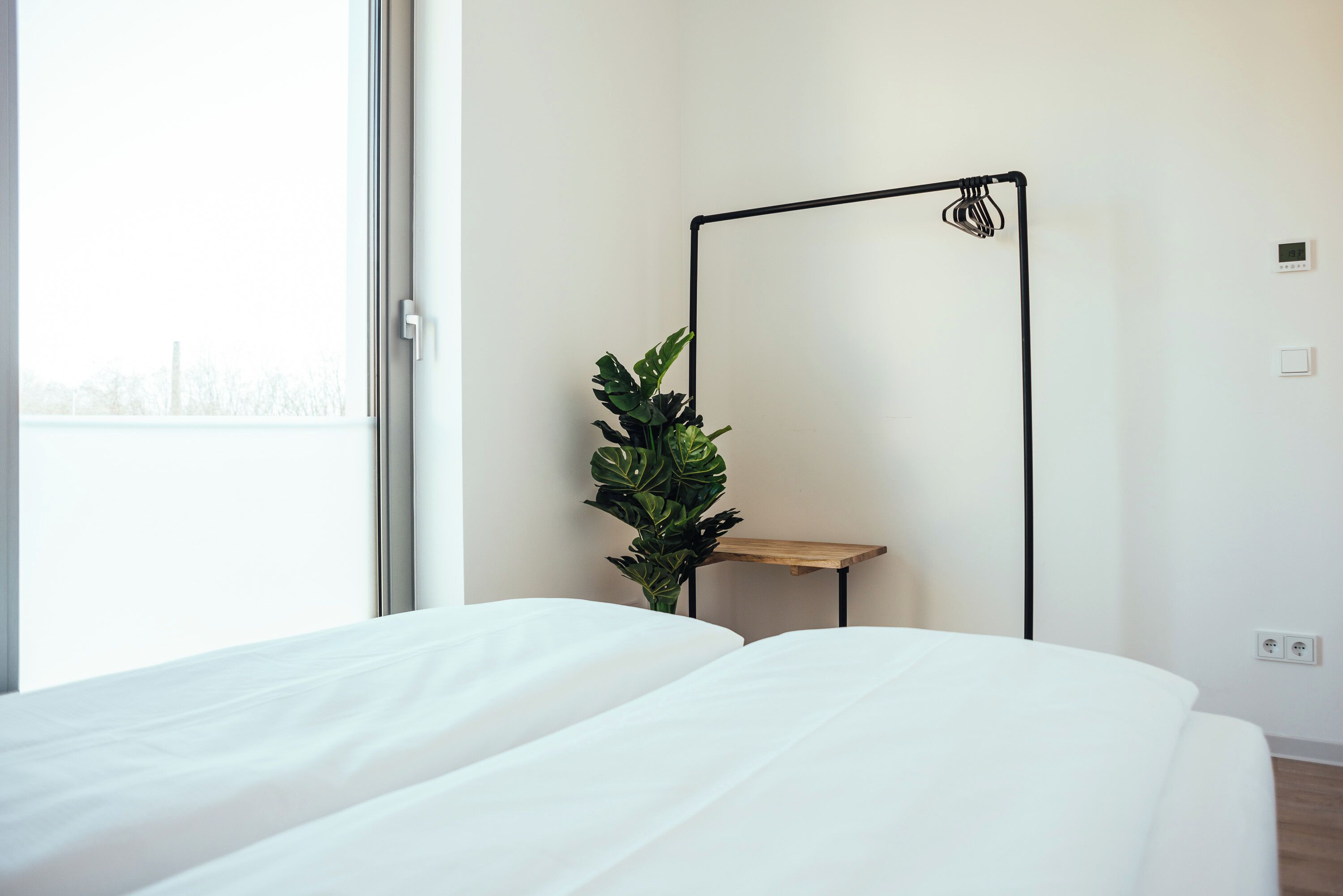 A bedroom with a large window, a bed, a plant, and a floor lamp.