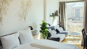 Ein modernes Schlafzimmer mit einem Bett, einem Sofa, einem kleinen runden Tisch und einem großen Fenster mit Vorhängen.