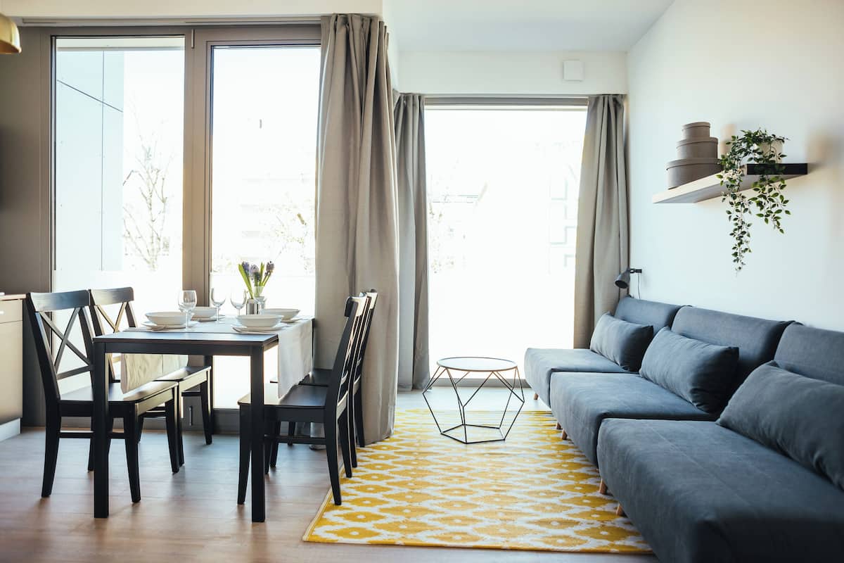 Una sala de estar moderna con un sofá gris, una mesa de comedor con sillas y un tapete amarillo estampado.