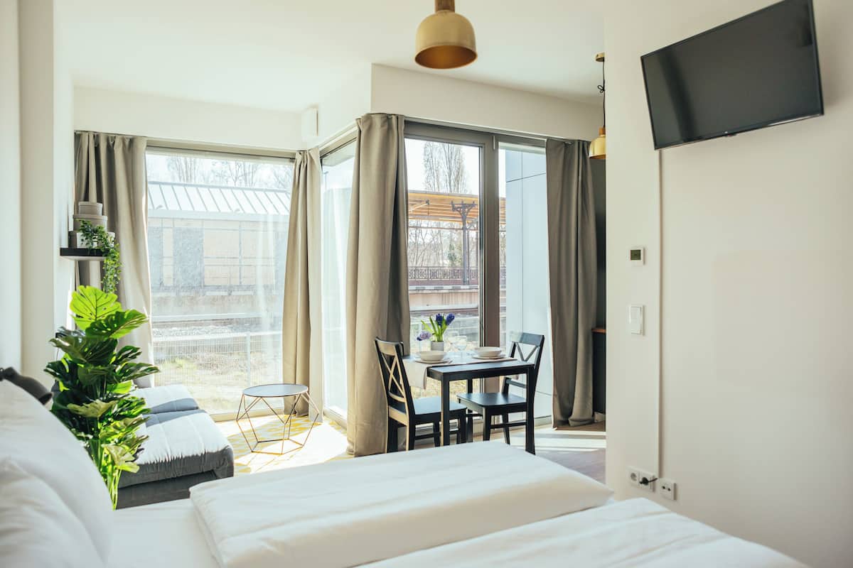 Una habitación de hotel moderna con una cama grande, una mesa de comedor con sillas, una pequeña mesa redonda y un televisor montado en la pared.