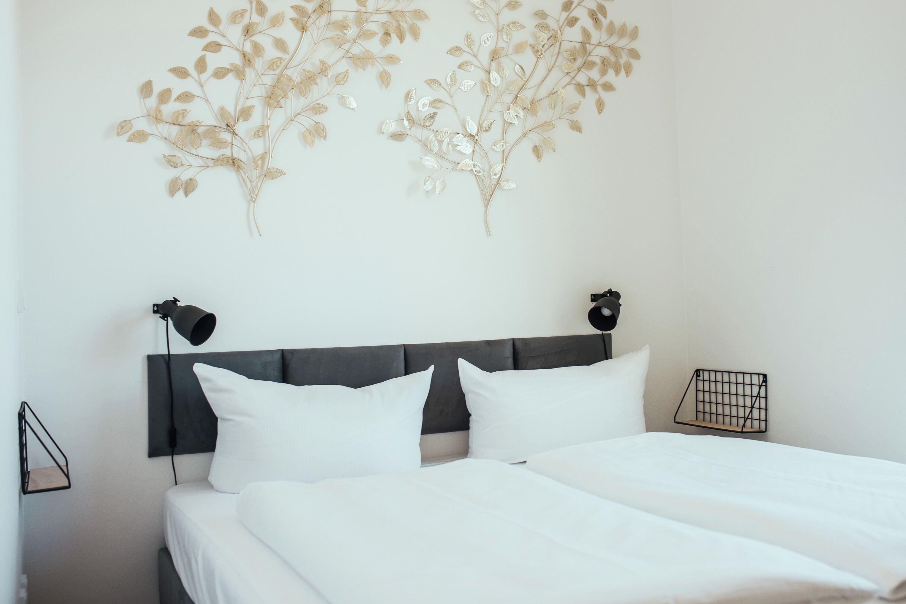 A neatly made bed with white linens, a dark headboard, and two wall-mounted lamps.