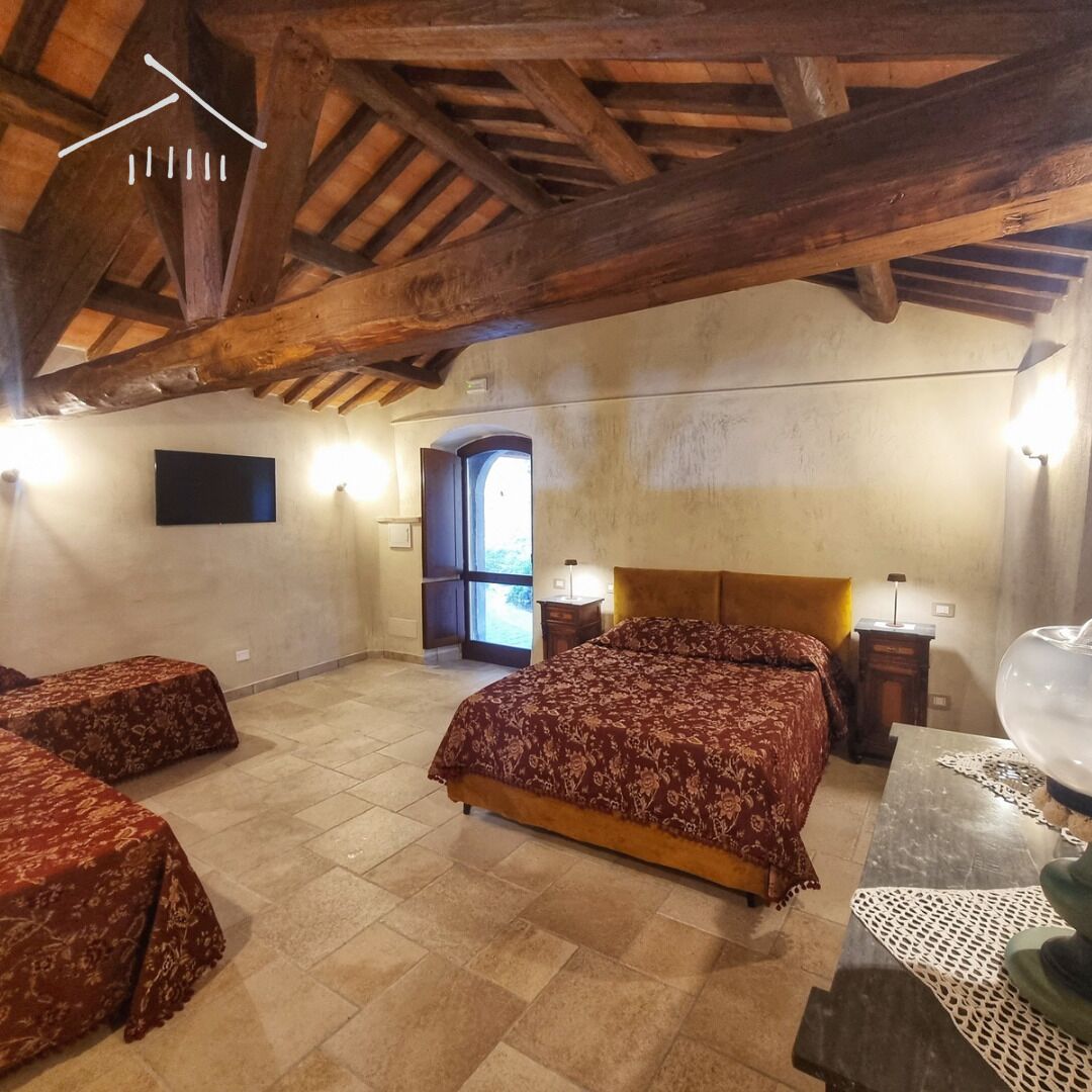Une chambre avec un grand lit, deux petits lits, des poutres en bois au plafond, un téléviseur fixé au mur et une fenêtre donnant sur un beau paysage.