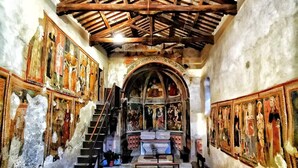 Un pasillo estrecho y tenuemente iluminado con techo de madera y paredes decoradas con frescos. Una escalera conduce a un altar al final.