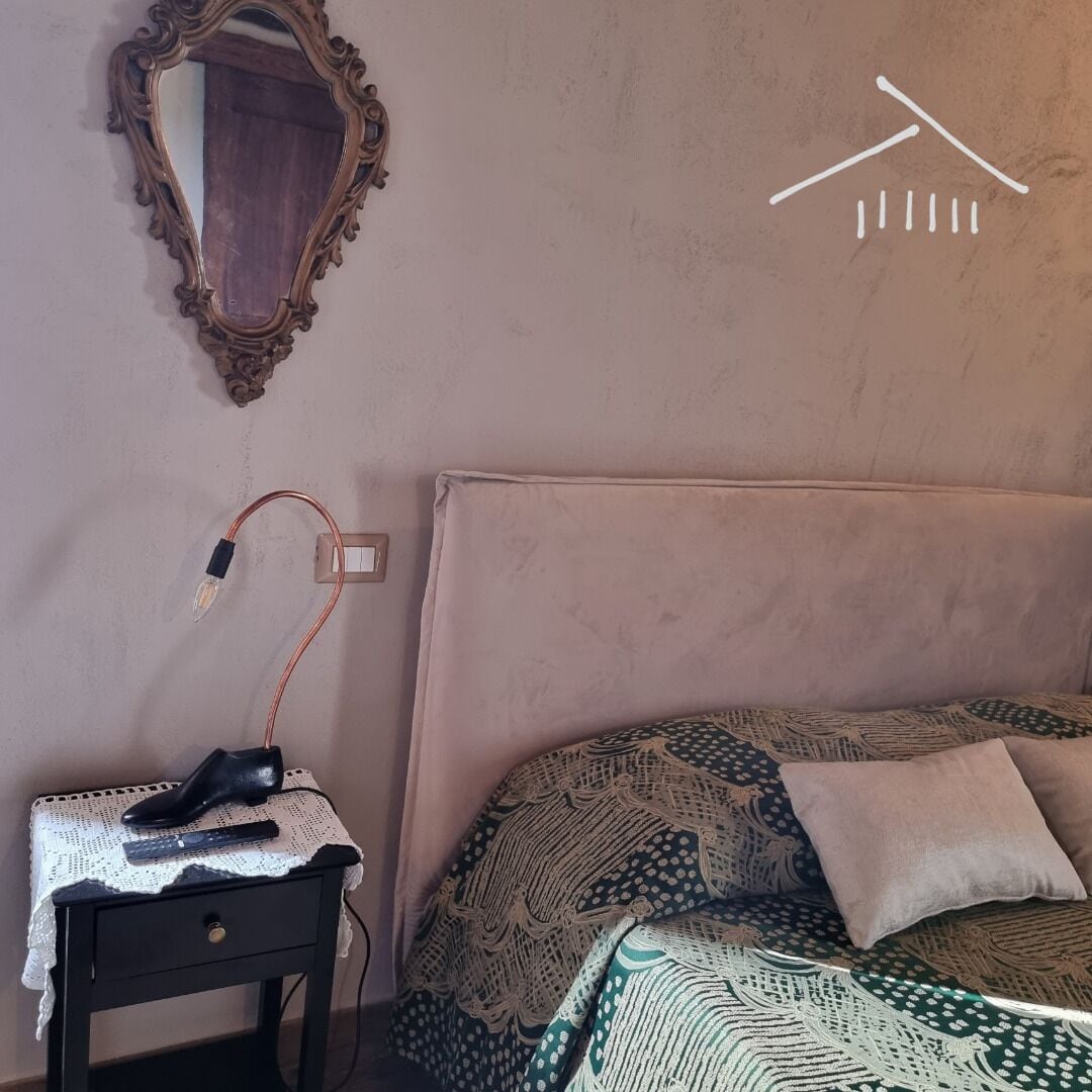 Una camera da letto con un letto, un comodino, una lampada, uno specchio e una presa a muro.