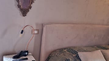 Una camera da letto con un letto, un comodino, una lampada, uno specchio e una presa a muro.