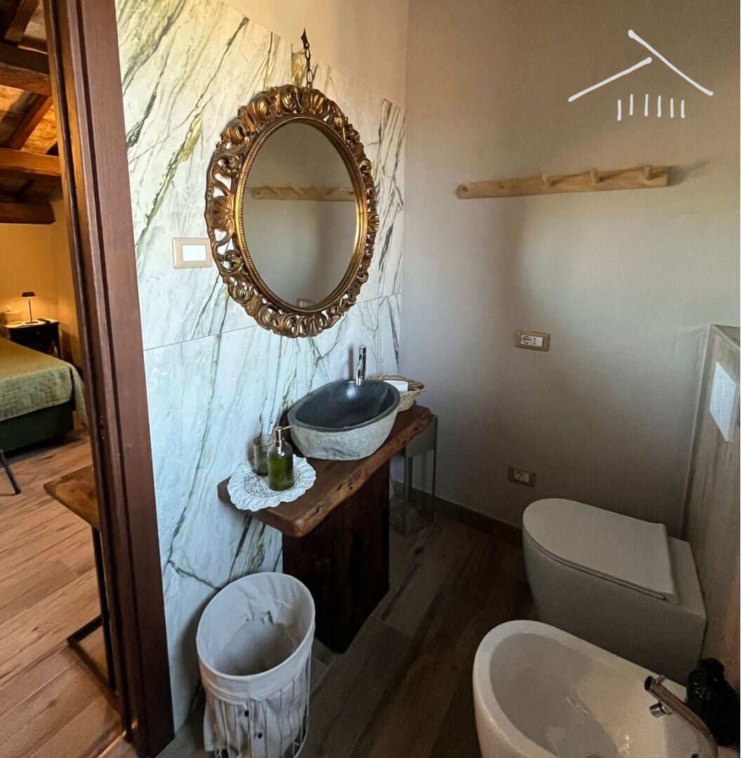 A bathroom with a marble wall, a freestanding sink, a toilet, and a bidet.