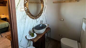 A bathroom with a marble wall, a freestanding sink, a toilet, and a bidet.