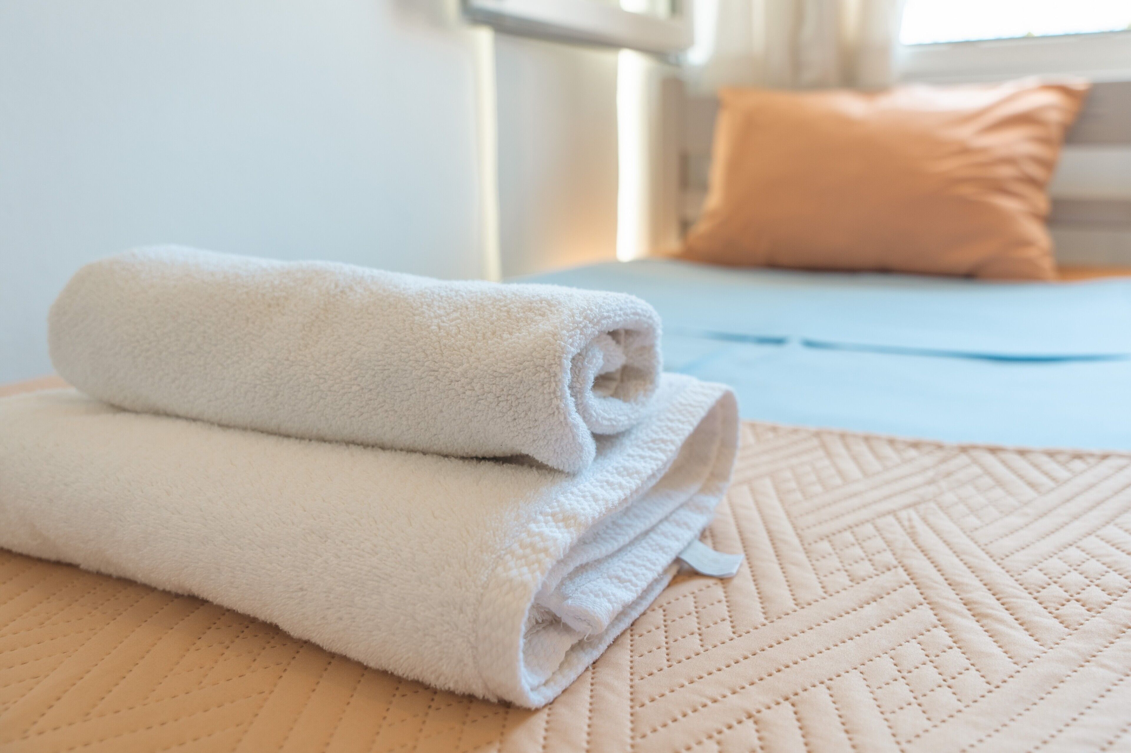 A neatly folded white towel on a beige quilted bedspread.