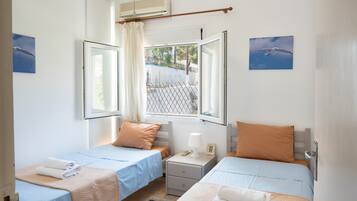 A room with two beds, a window with a view, a bedside table with a lamp, and a wall-mounted air conditioner.