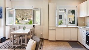 Une cuisine moderne avec des meubles blancs, une table à manger avec des chaises et de grandes fenêtres donnant sur l’extérieur.