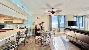 A modern living room with a dining area, a sofa, a TV, and a view of the ocean.