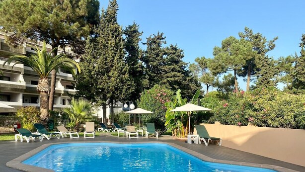 A swimming pool with lounge chairs and umbrellas, surrounded by trees and a building.