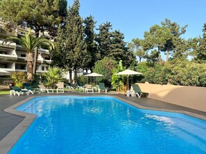 A swimming pool with lounge chairs and umbrellas, surrounded by trees and a building. - Villa "Balaia 9" with Shared Pool, Private Terrace and Wi-Fi (Olhos de Água)