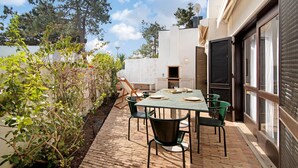 An outdoor patio with a table and chairs, a brick pathway, and a white wall with a door.