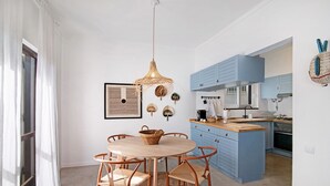 A modern kitchen with blue cabinets, a round wooden table with chairs, and a hanging woven light fixture.
