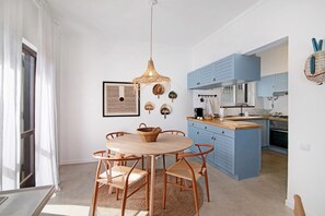 A modern kitchen with blue cabinets, a round wooden table with chairs, and a hanging woven light fixture.