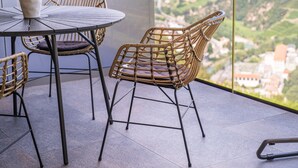 Een balkon met een ronde tafel en rieten stoelen, met uitzicht op een mooi landschap.