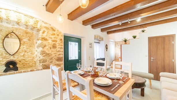 A dining area with a wooden table set for four, surrounded by white chairs with woven seats. A stone wall and a green door are visible in the background. - Bekiris Traditional Inn Country House with Private Terrace, Air Conditioning & Wi-Fi (Lefkimi)