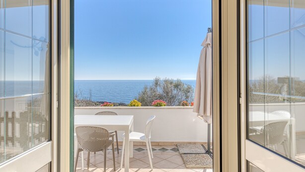 Een balkon met uitzicht op de zee, wit meubilair en een betegelde vloer.