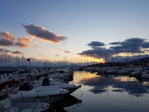 En lysthavn med flere både i havnen, roligt vand og en solnedgang i baggrunden.