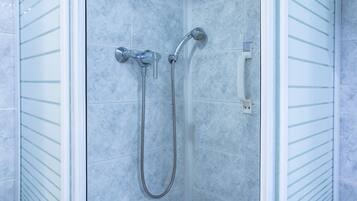 Une douche équipée d’un pommeau de douche à main et d’un pommeau de douche fixe, tous deux fixés au mur, et dont le sol est carrelé.